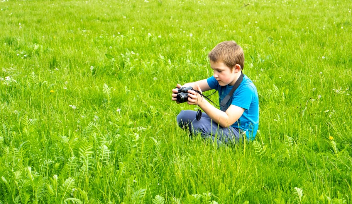Young boy exploring nature with a camera in green grass