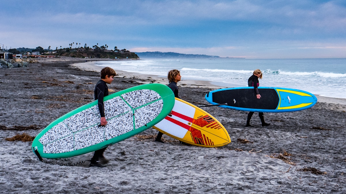 Group of friends carrying surfboards along a tropical beach
